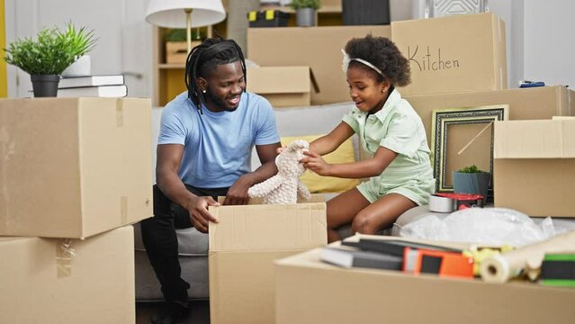 African american father and daughter unpacking teddy bear of cardboard box at new home