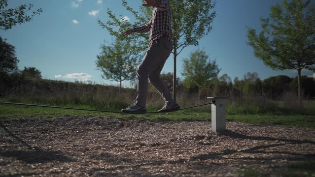 Man in sneakers learns walk and balance on balancing rope from rubber in a park in Germany. Sport, leisure, recreation and healthy active lifestyle concept. Beginner balances outdoors on slack line. 