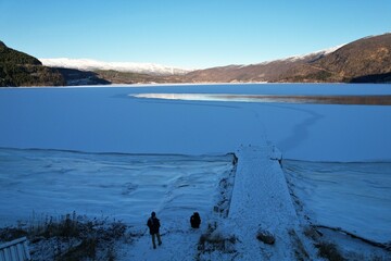 Observers by a dock witness the frozen stillness of a Norwegian lake