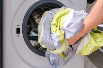 A woman opens the front door of a washing machine and puts clothes into the washing machine to clean and disinfect. Clean and healthy concept	