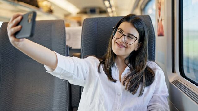 Young beautiful hispanic woman smiling taking a selfie picture with the smartphone sitting at train station