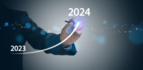 A businessman draws rising curve on virtual tech screen, from the end of 2023 rises to the start of...