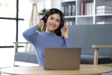 Young Asian woman wearing headphones listening to music in the living room at home.