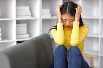 Young Asian woman with sickness and fever sitting on sofa at home. Young woman with depressed, depressed, worried and stressed.