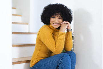 Happy african american woman sitting on stairs with folded hands at home, copy space - obrazy, fototapety, plakaty