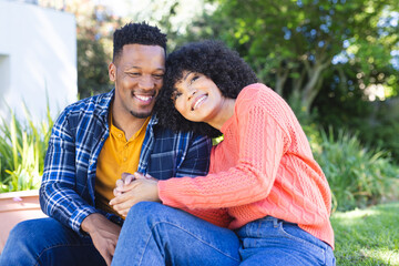 Fototapeta premium Happy african american couple embracing and holding hands on stairs in sunny garden, copy space