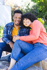 Happy african american couple embracing and holding hands on stairs in sunny garden, copy space