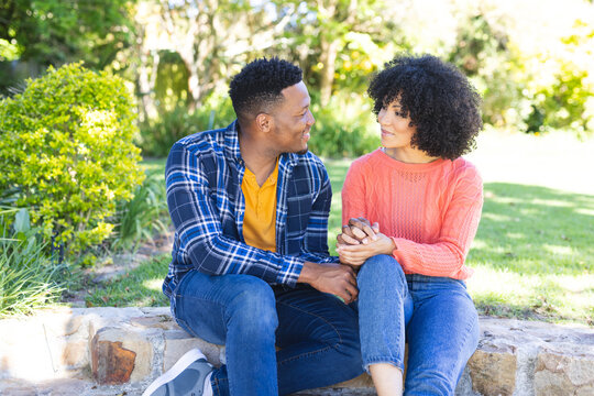 Happy african american couple sitting on stairs and holding hands in sunny garden, copy space