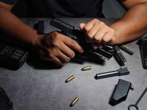 Gunsmith cleaning pistol Assemble, dismantle, and maintain with a brush to clean a black 9 mm pistol on an old cement floor pattern table. Gun maintenance gear.