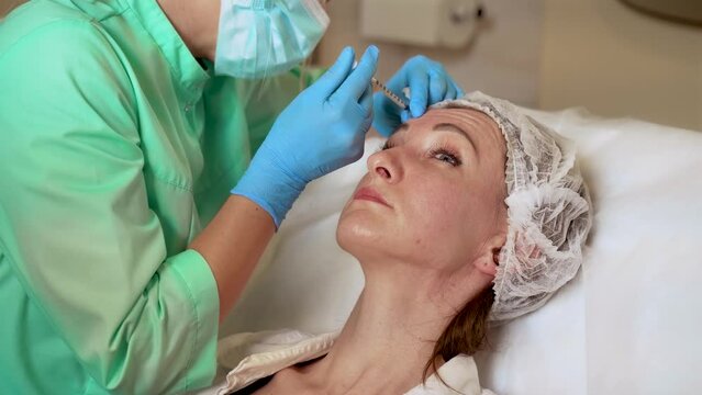 Face woman getting beauty injection in cosmetic clinic. Close up cosmetologist doing neurotoxin injection in forehead to patient in beauty clinic. Cosmetology cabinet, medical procedures, skin