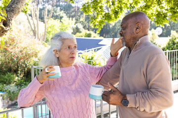 Diverse senior couple drinking coffee and talking on sunny terrace