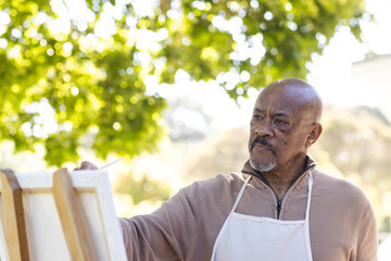 African american senior man painting on canvas on sunny terrace