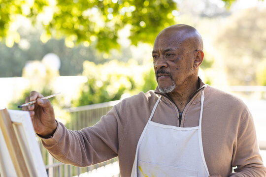 African american senior man painting on canvas on sunny terrace - Powered by Adobe