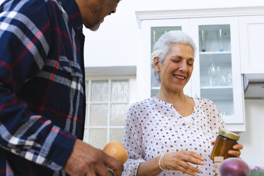 Happy diverse senior couple unpacking groceries in kitchen - Powered by Adobe