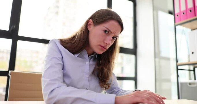 Suspicious female manager typing on keyboard in office and looking at camera