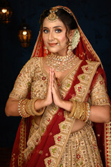 Stunning Indian bride dressed in traditional bridal lehenga with heavy gold jewellery and veil,...