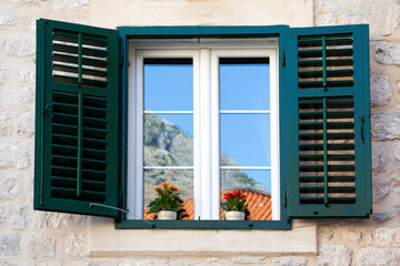a typical window with louvered shutters and square paned windows with flowers in hanging flower pots