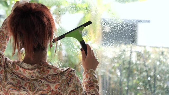 Beautiful young woman cleaning window at home