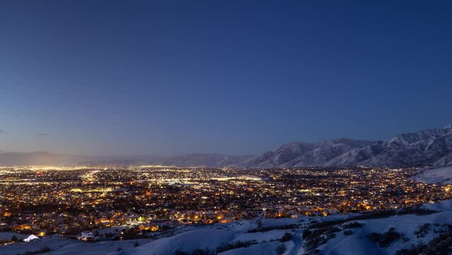 Time lapse of city lights and snow covered Wasatch Mountains at sunset. Salt Lake City, Utah.