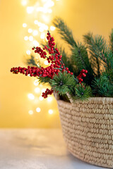 Wicker basket with christmas fir branches and red ilex flower with bokeh lights on background, decoration at home