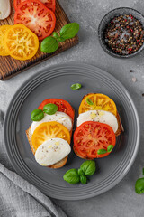 Sandwich caprese with rye bread, tomatoes, mozzarella and fresh basil on a gray plate on a concrete background. Healthy food.