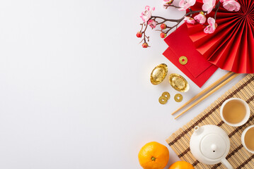 Step into elegance of Chinese New Year celebration through top-view table setting. Highlighting ornamental fan, green tea setup, placemat, Feng Shui symbols, tangerines, etc on white backdrop for text
