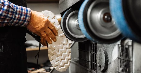 Poster Handwerker, Schuster arbeitet hält einen Schuh und schleift die Sohle an Schleifmaschine. Im Vordergrund steht ein Lederschuh, unscharf. Querformat © Sonja