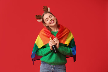 Young woman in reindeer horns with LGBT flag and champagne on red background