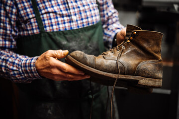 Ein Schuster, Schuhmacher, Handwerker hält einen alten, kaputten Schuh aus Leder in seinen...