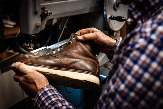 Schuster, der einen alten Schuh in den H&auml;nden h&auml;lt und an der N&auml;hmaschine reparieren will
