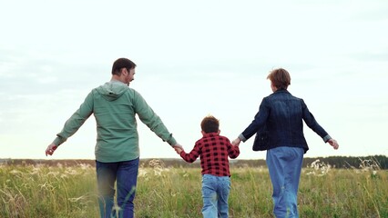 Parents and son energetically run holding each other hands across open field