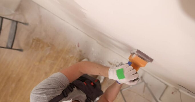 Home improvement plasterer working with grinder to level surface of wall. Wall repair and preparation for painting