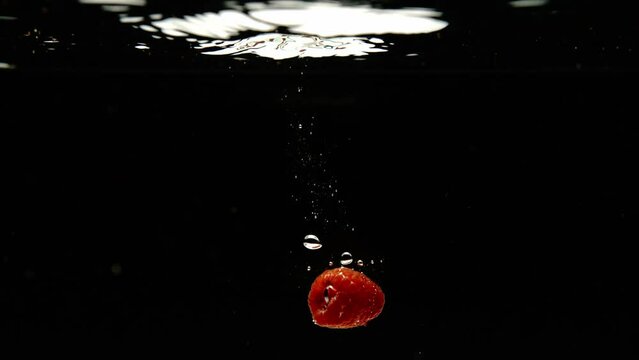 Super slow motion of falling fresh raspberries into water on black background. Filmed on high speed cinema camera, 600 fps.