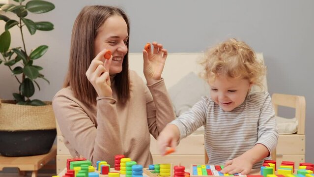 Developmental toys. Infant creativity. Shape sorter. Emotional intelligence. Caucasian woman playing with her infant baby in home interior covering eyes with round details.