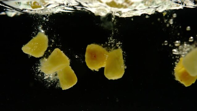 Super slow motion of fresh mango and pineapple falling into water on black background. Filmed on high speed cinema camera, 600 fps.