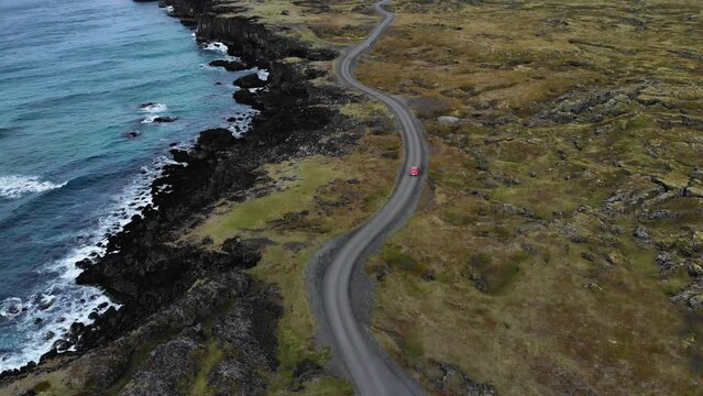Aerial of a red car driving on a bendy road at the coastline of Iceland
