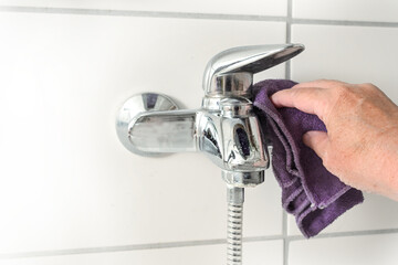 Hand with a microfiber cloth cleaning an old bathtub faucet full of limescale stains caused by hard calcium water, copy space, selected focus