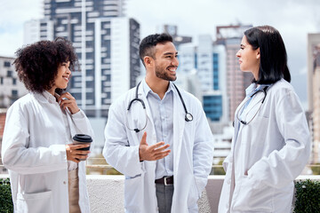 Fototapeta premium Happy, doctors and talking of healthcare on coffee break, outdoor and relax at hospital, clinic or colleagues on rooftop. Surgeon, smile and enjoy drink on balcony with staff and work in medicine