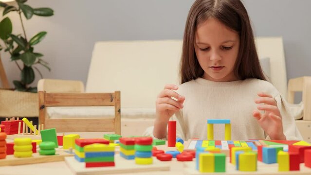 Little dark haired female kid playing with sorter toys educational boards for color and shapes sorting girl spending time at home with geometrics figures games.