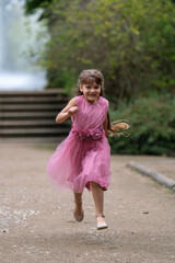 A little cute girl in a beautiful pink dress with long hair runs quickly. Outdoor games. Blurred background.