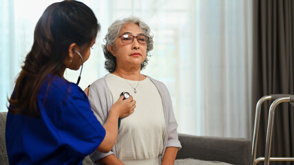 Doctor using stethoscope and listening senior woman heartbeat during home visit. Health care concept