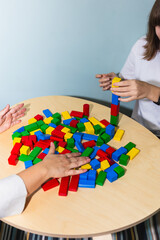 An unrecognizable adolescent patient and her psychotherapist's hands playing with colored wooden blocks in therapy session. Concept of therapy and mental health