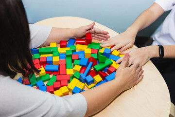 Hands of an adolescent patient and her psychotherapist picking up colored wooden blocks in therapy....