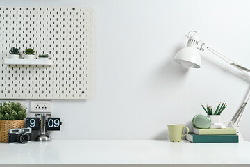 Comfortable workplace with books, lamp, camera, clock and pegboard on white wall