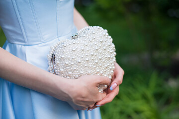 Woman wearing a formal blue satin dress holding a heart-shaped handbag with pearls - detail,...