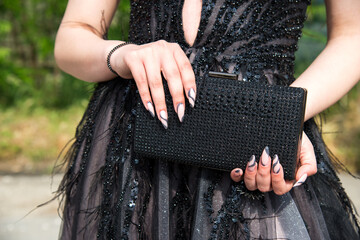 Close-up of a woman wearing a formal black dress, her hands with an attractive manicure, holding a...