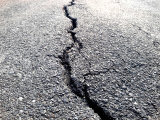 Cracked asphalt surface cracks. Post-earthquake damage. There were long, rough, winding cracks in...