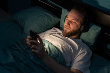 Handsome mobile addict man using smartphone browsing the internet for watching movie or virtual meeting video call online with girlfriend on the bed, sleep time at night. - obrazy, fototapety, plakaty