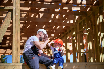 Father with toddler son building wooden frame house. Man giving high five to kid, having fun on the...