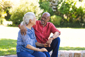 Happy diverse senior couple embracing and sitting on stairs in sunny garden